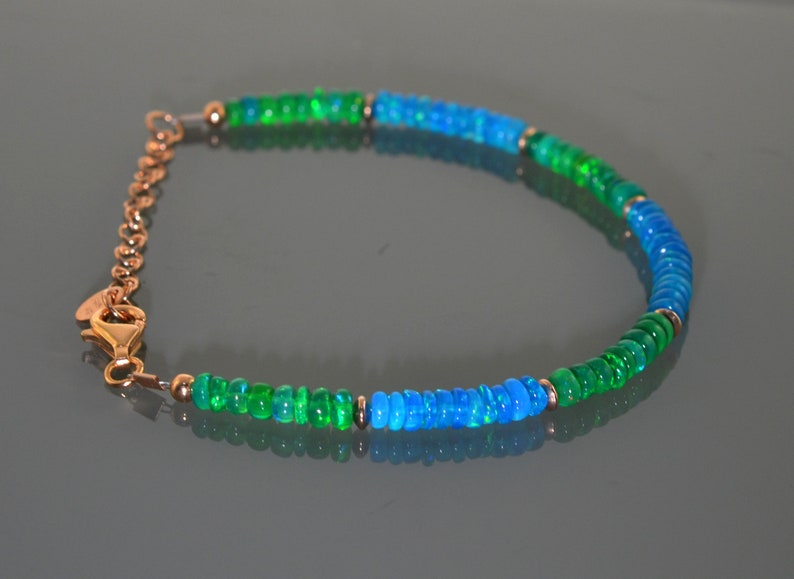 Pu&ograve; includere: Un braccialetto con perline di opale verde e blu con una chiusura dorata.