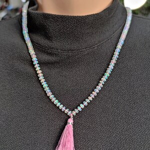 Pode incluir: Um colar feito de contas de opala iridescente com um pingente de borla rosa.