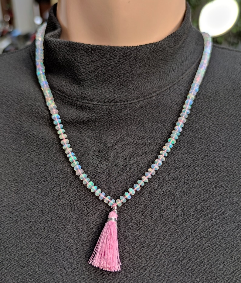 Pode incluir: Um colar feito de contas de opala iridescente com um pingente de borla rosa.
