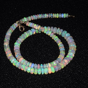 May include: A necklace made of iridescent opal beads. The beads are a mix of light and dark shades of blue, green, and pink. The necklace is strung on a silver chain.