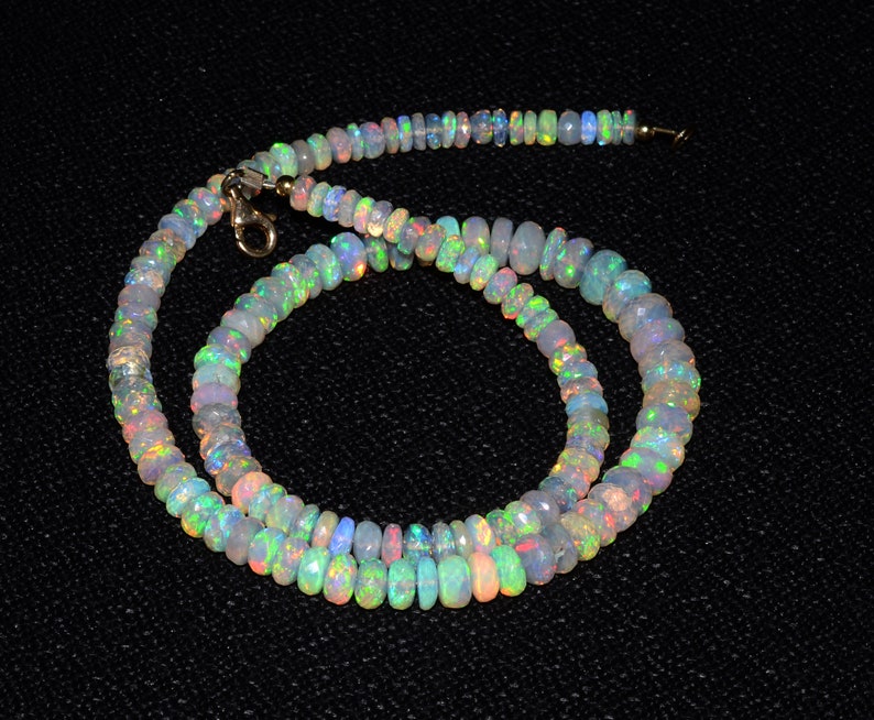 May include: A necklace made of iridescent opal beads. The beads are a mix of light and dark shades of blue, green, and pink. The necklace is strung on a silver chain.