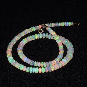 May include: A multi-colored opal bead necklace with a gold clasp. The necklace is made of small, round beads that are strung together on a thin gold chain.