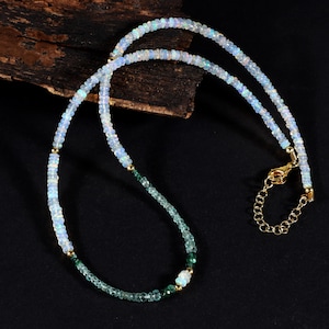 May include: A delicate necklace with white opal and green gemstone beads. The necklace has a gold clasp and is layered with two strands of beads.