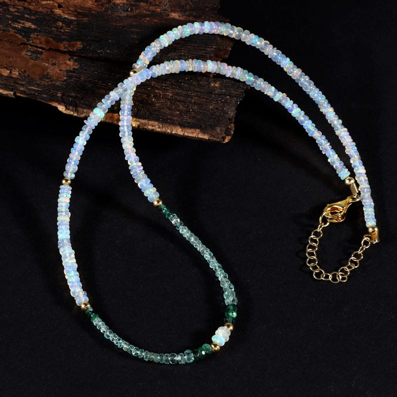 May include: A delicate necklace with white opal and green gemstone beads. The necklace has a gold clasp and is layered with two strands of beads.