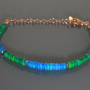 Pu&ograve; includere: Un braccialetto con perline di opale verde e blu con una chiusura dorata. Il braccialetto &egrave; fatto di piccole perline rotonde che sono infilate su una catena d'oro.