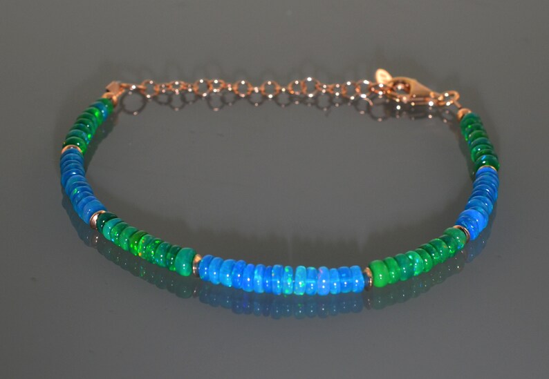 Pu&ograve; includere: Un braccialetto con perline di opale verde e blu con una chiusura dorata. Il braccialetto &egrave; fatto di piccole perline rotonde che sono infilate su una catena d'oro.