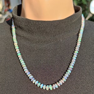 Pode incluir: Um colar feito de contas de opala ovaladas iridescentes. O colar est&aacute; sobre um fundo preto.