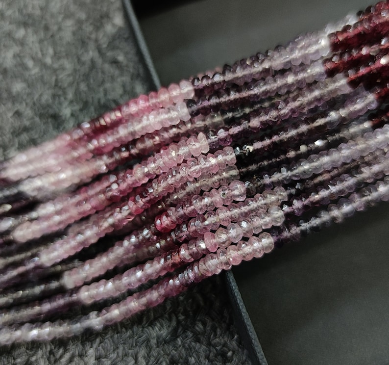 May include: A strand of pink and purple gemstone beads. The beads are faceted and have a slightly irregular shape. The beads are strung on a clear thread.