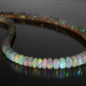 May include: A strand of iridescent opal beads, each bead is a different shade of white, green, and blue. The beads are strung on a clear thread and are arranged in a circular pattern.
