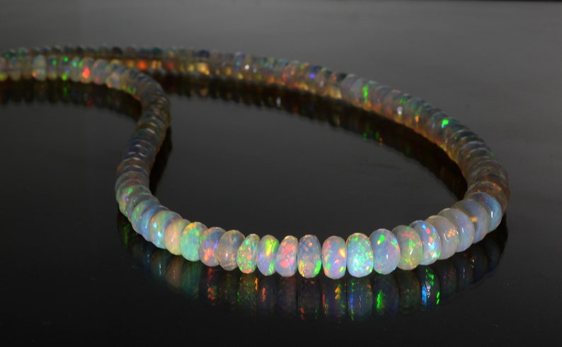 May include: A strand of iridescent opal beads, each bead is a different shade of white, green, and blue. The beads are strung on a clear thread and are arranged in a circular pattern.