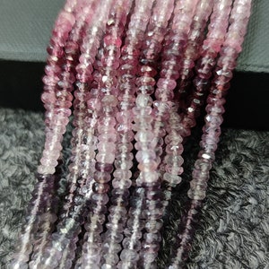 May include: A strand of pink and purple gemstone beads. The beads are faceted and have a gradient color from dark purple to light pink.