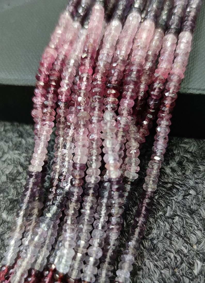 May include: A strand of pink and purple gemstone beads. The beads are faceted and have a gradient color from dark purple to light pink.