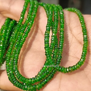 May include: A strand of small, faceted, vibrant green gemstone beads. The beads are uniform in size and shape, featuring a polished, reflective surface that catches the light. The strand is arranged in multiple loops, showcasing the consistent deep green color and the intricate, multi-faceted cut of each individual bead throughout the entire length of the string.