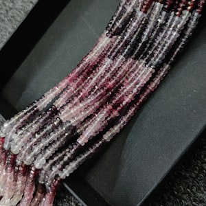 May include: A strand of pink, purple, and white gemstone beads. The beads are faceted and have a slightly irregular shape. The beads are strung on a clear thread.