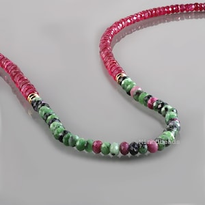 Op de afbeelding: Een kralenketting met een lange streng gefacetteerde dieprode robijnkralen die overgaat in een sectie van veelkleurige zoisietkralen met groene, zwarte en roze tinten. Kleine goudkleurige metalen tussenstukjes scheiden de kraalsegmenten.