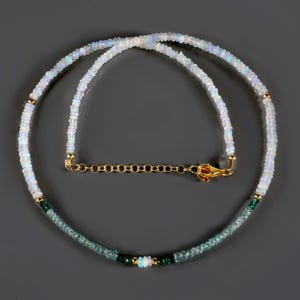 May include: A delicate necklace made with white opal and green gemstone beads. The necklace has a gold chain clasp.