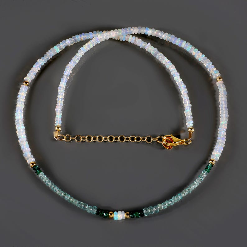 May include: A delicate necklace made with white opal and green gemstone beads. The necklace has a gold chain clasp.