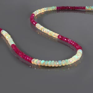 May include: A necklace made of white opal and ruby beads. The necklace is made of alternating colors of white opal and ruby beads.