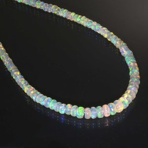 Pode incluir: Um colar de contas de opala branca com reflexos arco-&iacute;ris iridescentes. As contas s&atilde;o redondas e lisas, e o colar mede aproximadamente 45 cm de comprimento.