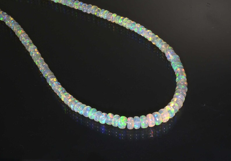 Pode incluir: Um colar de contas de opala branca com reflexos arco-&iacute;ris iridescentes. As contas s&atilde;o redondas e lisas, e o colar mede aproximadamente 45 cm de comprimento.