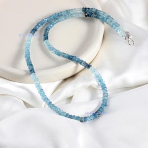 May include: A beaded necklace featuring small, faceted, round gemstones in a gradient of blue shades, ranging from pale sky blue to deep navy. The strand is finished with a silver-toned metal clasp at one end, creating a continuous loop.