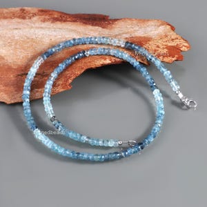 May include: A necklace composed of small, faceted, round blue gemstone beads that transition in color from light sky blue to deep navy blue. The strand features a silver-toned metal lobster claw clasp and small silver-toned metal spacer beads.