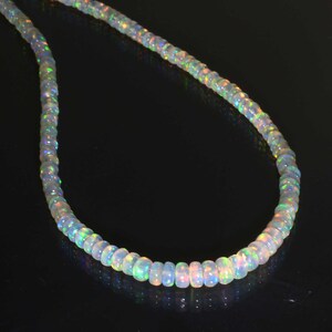 Pode incluir: Um colar de contas de opala branca com cores arco-&iacute;ris iridescentes. O colar &eacute; feito de pequenas contas redondas que s&atilde;o enfiadas em um cord&atilde;o fino.