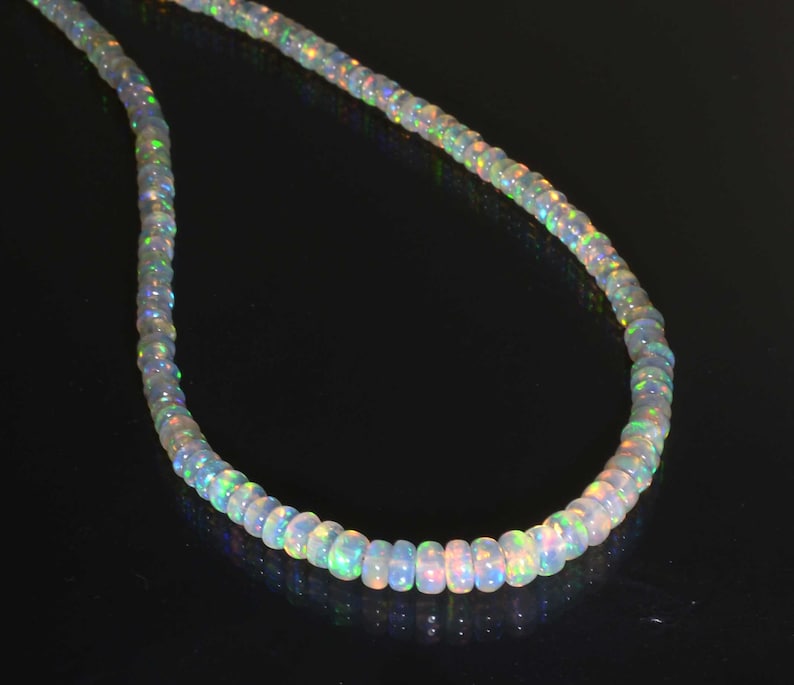 Pode incluir: Um colar de contas de opala branca com cores arco-&iacute;ris iridescentes. O colar &eacute; feito de pequenas contas redondas que s&atilde;o enfiadas em um cord&atilde;o fino.