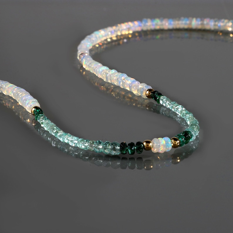 May include: A white opal and green gemstone beaded necklace. The necklace is made with small, round beads and features a gold accent.
