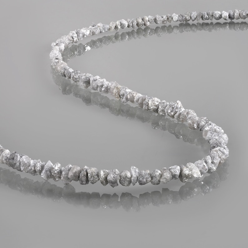 May include: A strand of rough, unpolished, gray diamonds strung together on a thin, clear thread. The diamonds are various sizes and shapes, creating a unique and natural look.