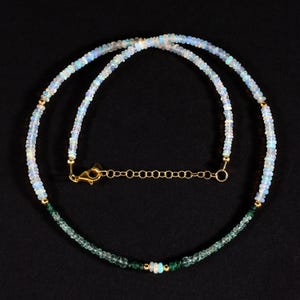 May include: A delicate necklace made with white opal beads and green gemstone beads. The necklace has a gold clasp and chain.