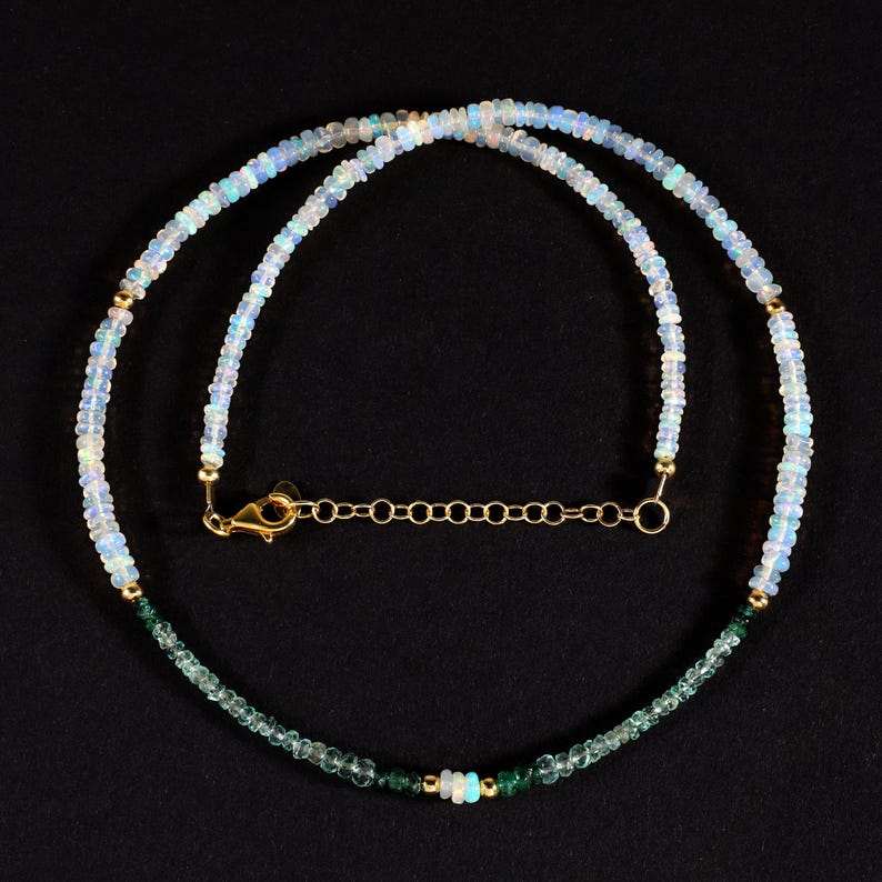 May include: A delicate necklace made with white opal beads and green gemstone beads. The necklace has a gold clasp and chain.