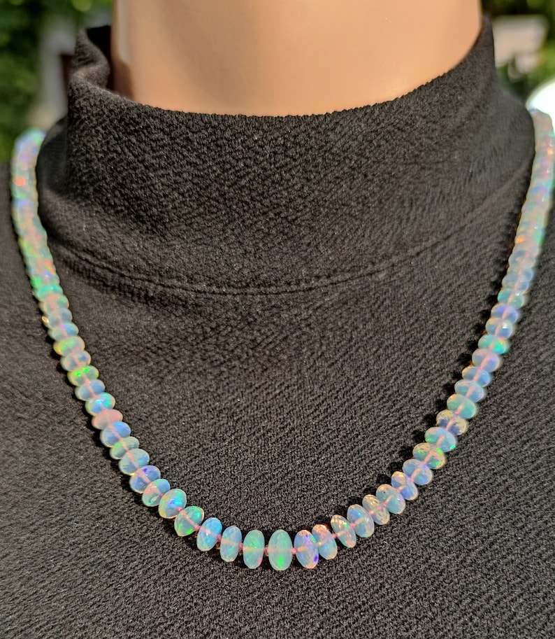 Pode incluir: Um colar feito de contas de opala branca iridescente. As contas s&atilde;o de forma oval e enfiadas em uma corrente de prata.