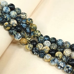 May include: A strand of round, blue, black, and brown agate beads with a speckled pattern. The beads are strung on a clear thread.