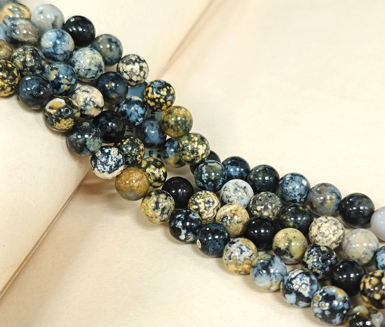 May include: A strand of round, blue, black, and brown agate beads with a speckled pattern. The beads are strung on a clear thread.
