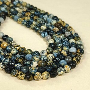 May include: A strand of blue, brown, and white speckled round beads. The beads are made of natural stone and have a mottled appearance.