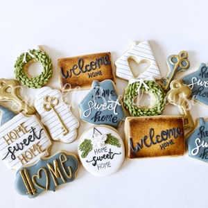 Puede incluir: Surtido de galletas decoradas con dise&ntilde;os tem&aacute;ticos de hogar. Las galletas incluyen formas de casa, llaves, coronas y letreros con frases como "Welcome Home" y "Home Sweet Home". Los colores incluyen dorado, blanco y tonos de azul y verde.