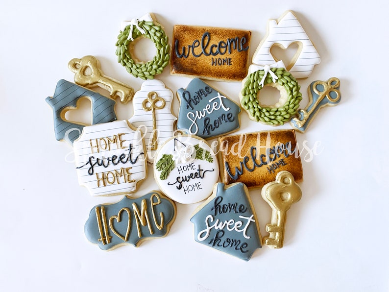 Puede incluir: Una variedad de galletas decoradas con formas de llaves, casas y coronas. Las galletas est&aacute;n adornadas con las frases "Welcome Home" y "Home Sweet Home" en una elegante escritura, con detalles dorados y azules.