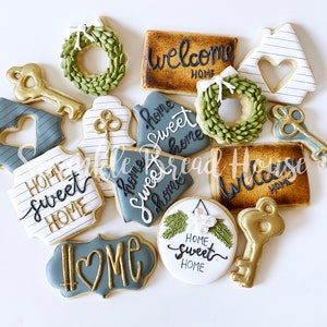 Puede incluir: Un surtido de galletas decoradas con tem&aacute;tica de hogar. Las galletas tienen varias formas, incluyendo llaves, casas y coronas. Algunas galletas tienen las palabras "Welcome Home" y "Home Sweet Home" escritas en glaseado negro con detalles dorados.