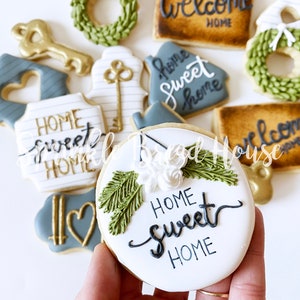 Puede incluir: Surtido de galletas de az&uacute;car decoradas con tem&aacute;tica de hogar. Las galletas incluyen formas de llaves, casas y coronas, con las frases "Home Sweet Home" y "Welcome Home" escritas en elegante caligraf&iacute;a. Los colores incluyen blanco, dorado, verde y gris.