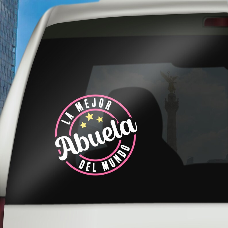 May include: A pink and white circle sticker with the text "La Mejor Abuela Del Mundo" and three yellow stars. The sticker is on a black background.