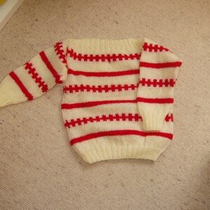 May include: A white and red striped knitted sweater with a boat neck.