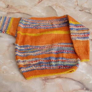 Può includere: Un maglione a righe arancione, giallo, blu e bianco.