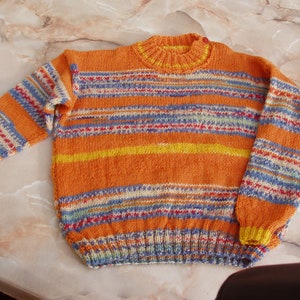 Può includere: Un maglione a righe arancione, giallo, blu e bianco.