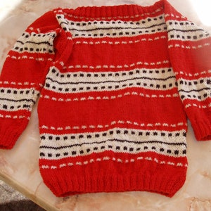 Può includere: Maglione rosso a maglia con strisce bianche e nere. Il maglione ha una scollatura ampia e maniche lunghe.