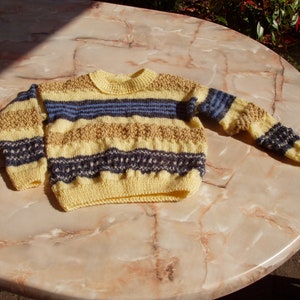 Può includere: Un maglione a righe gialle, marroni e blu con collo rotondo.