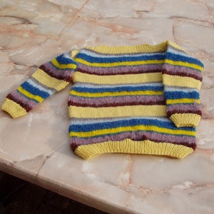Könnte beinhalten: Ein gestrickter Pullover mit Streifen in Gelb, Blau, Grau und Braun.