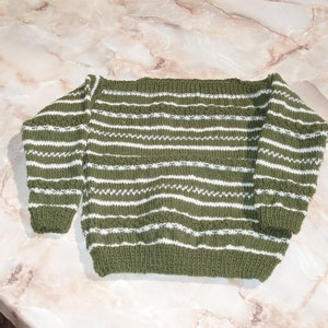 May include: A green and white striped knitted sweater with a wide neckline.