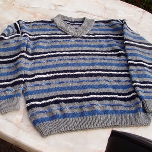 Könnte beinhalten: Ein gestreifter Pullover in den Farben Blau, Grau und Weiß. Der Pullover hat einen V-Ausschnitt und lange Ärmel.
