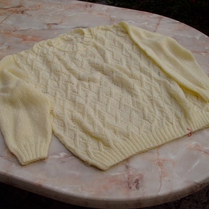 May include: A pale yellow knitted jumper with a diamond pattern. The jumper is made of a soft, lightweight yarn and has a relaxed fit.